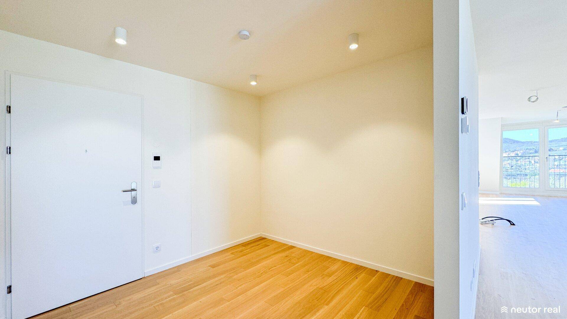 Heller Eingangsbereich mit Holzboden und weißer Tür, ausgestattet mit modernen Deckenstrahlern.