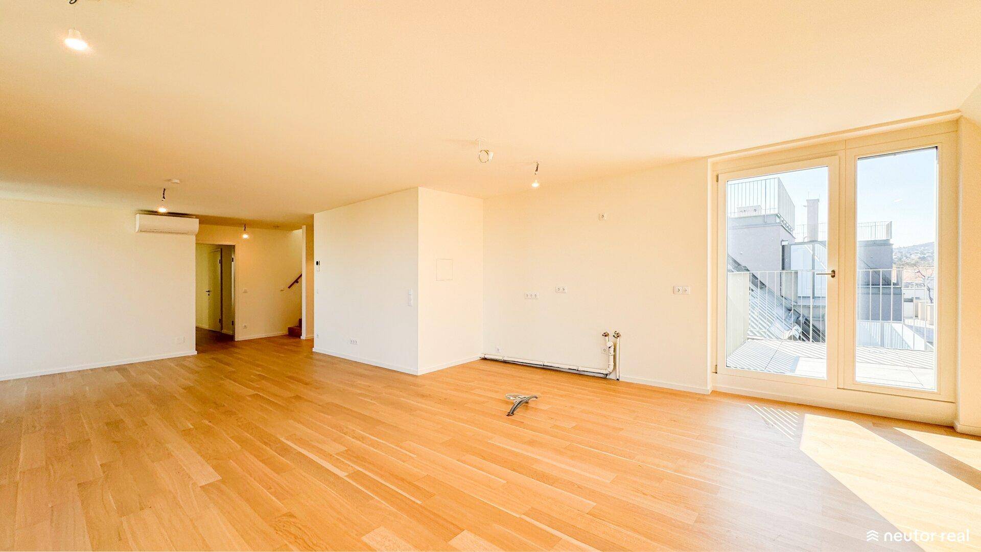 Weitläufiger Wohnbereich mit hellem Holzboden und großen Fenstern, die viel Licht spenden.