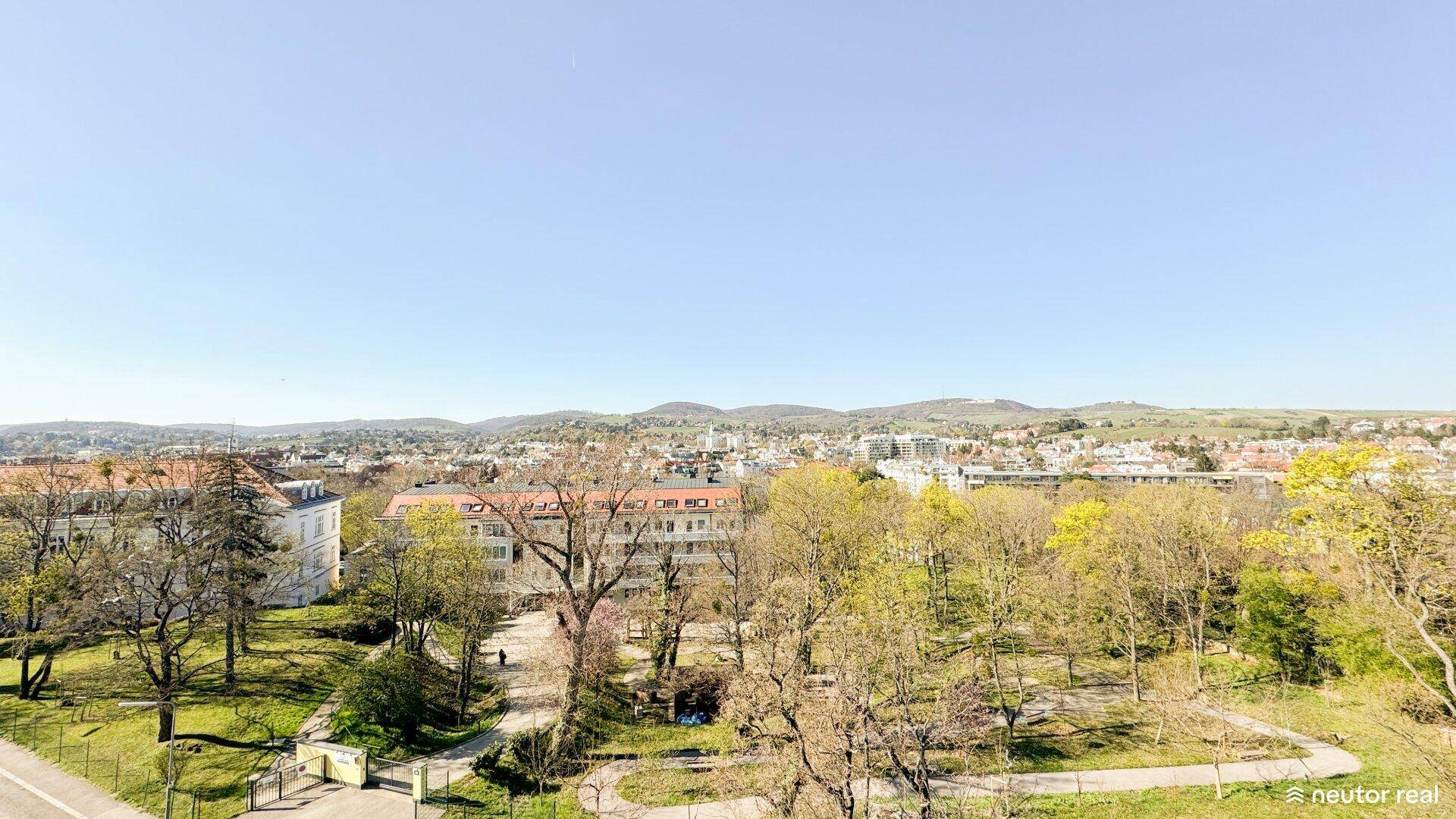 Panoramablick über einen grünen Park, die Stadt und die sanften Hügel in der Ferne.
