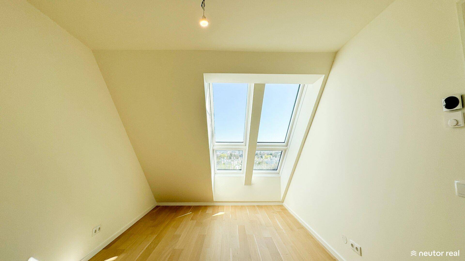 Helles Zimmer mit Holzboden und großem Dachfenster, das viel natürliches Licht spendet.