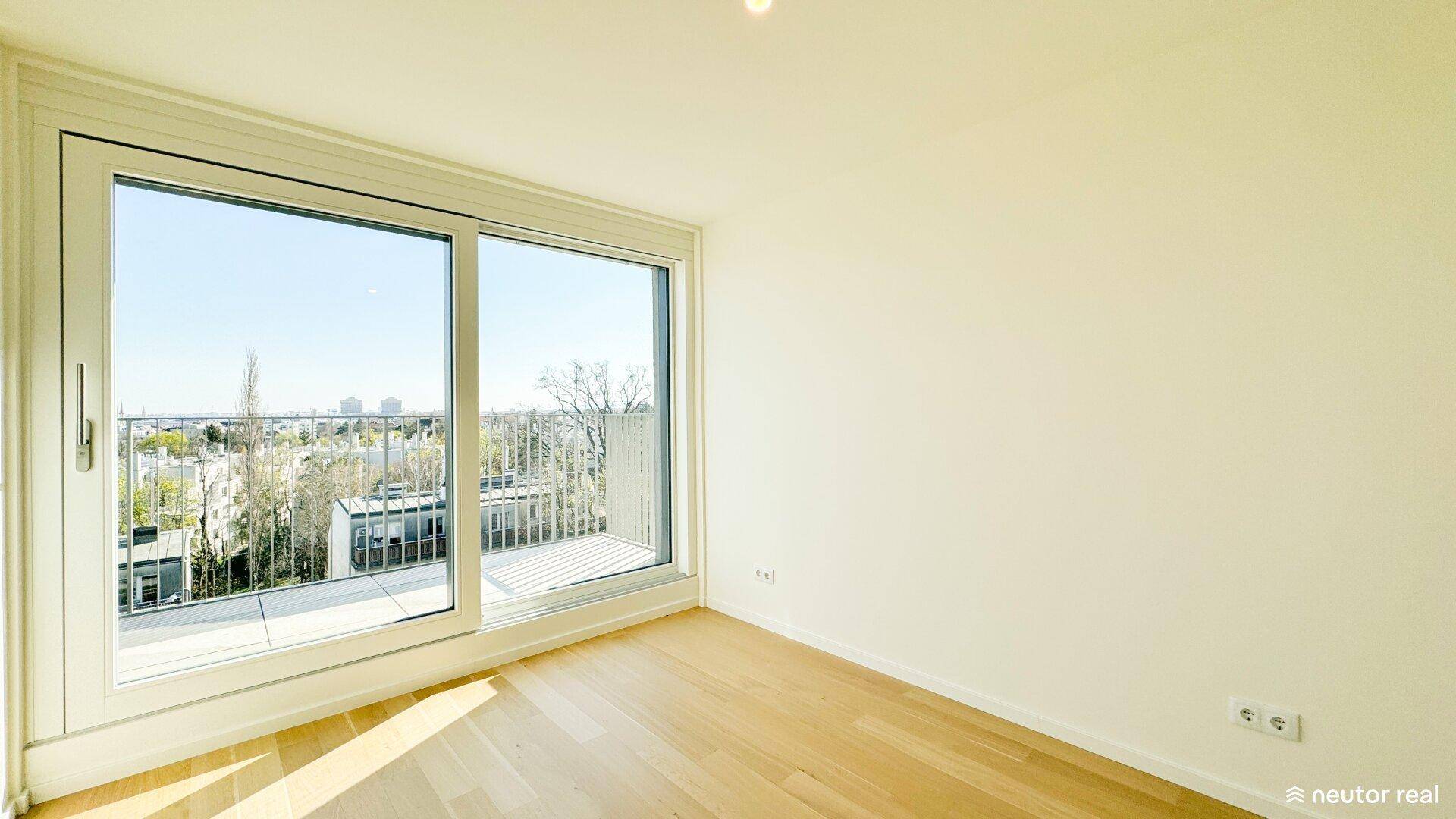 Schlafzimmer mit Holzboden und großer Schiebetür, die Zugang zu einem kleinen Balkon bietet und Stadtblick ermöglicht.
