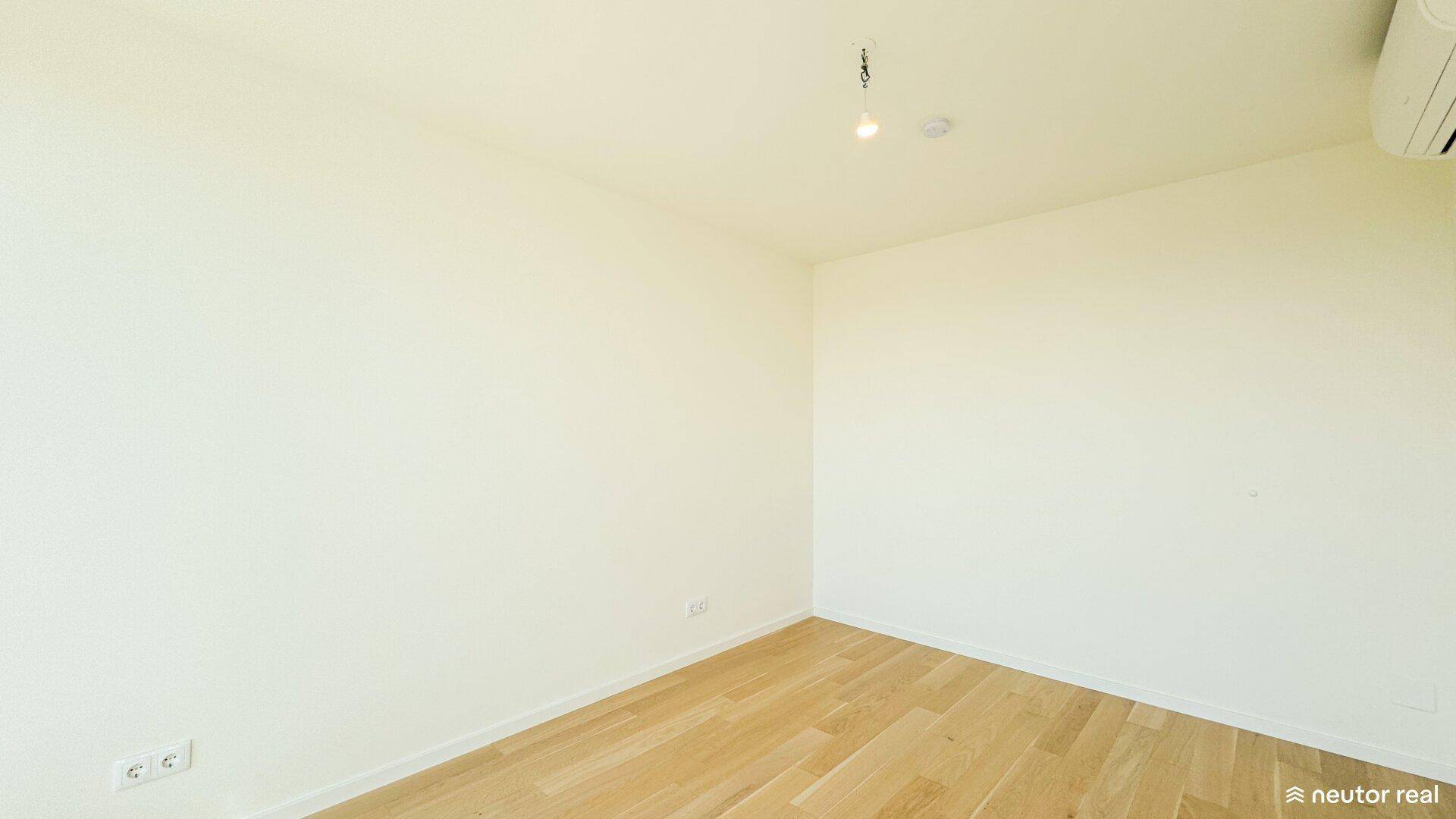 Leeres Schlafzimmer mit Holzboden und Klimaanlage, bereit zur individuellen Gestaltung.