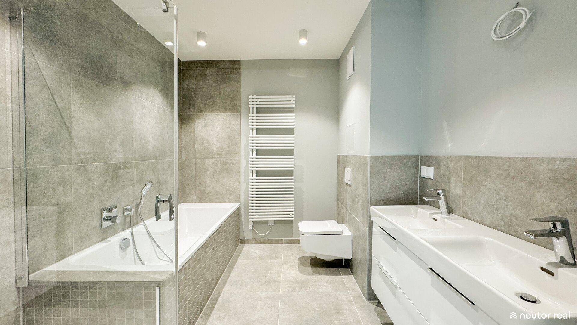 Modernes Badezimmer mit Badewanne, wandhängendem WC, beheiztem Handtuchhalter und Doppelwaschbecken.