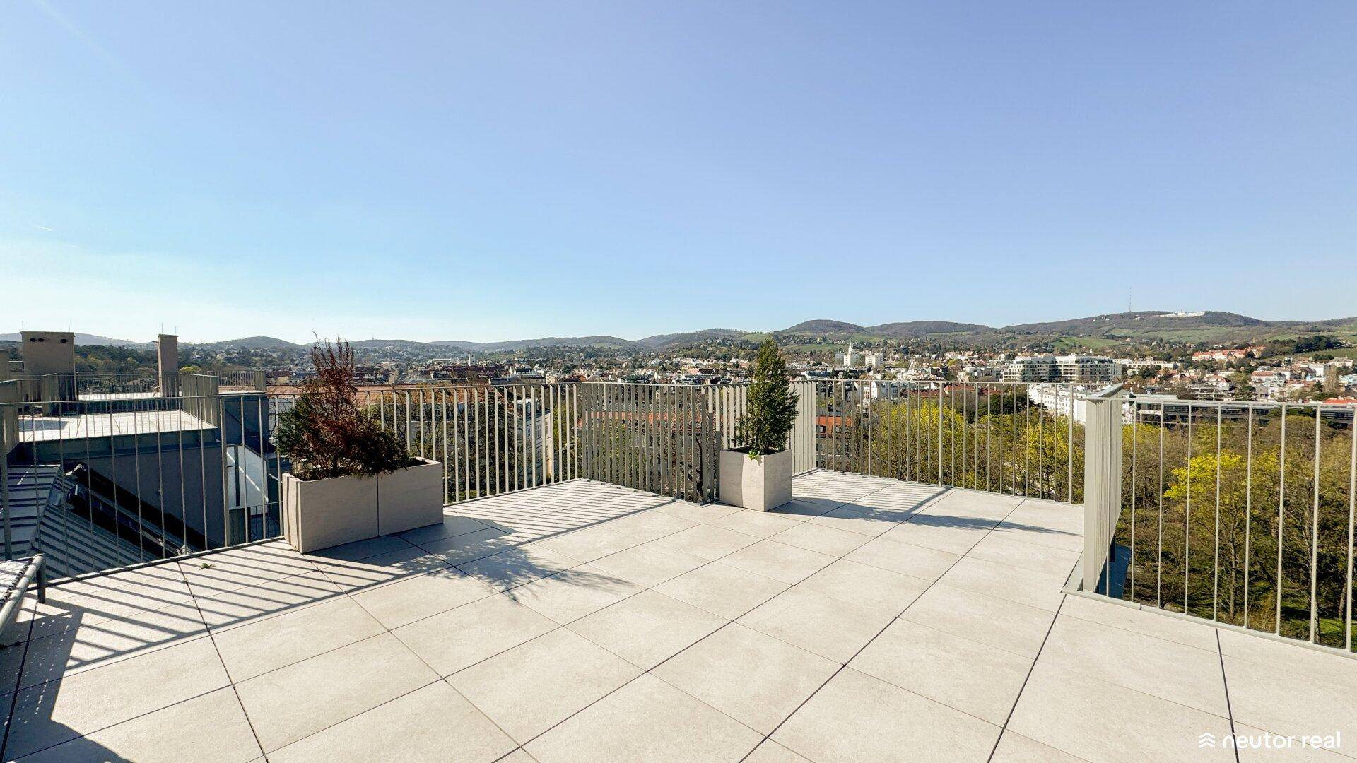 Weitläufige Dachterrasse mit Pflanzenkübeln und Panoramablick über die Stadt und die umliegenden Hügel.