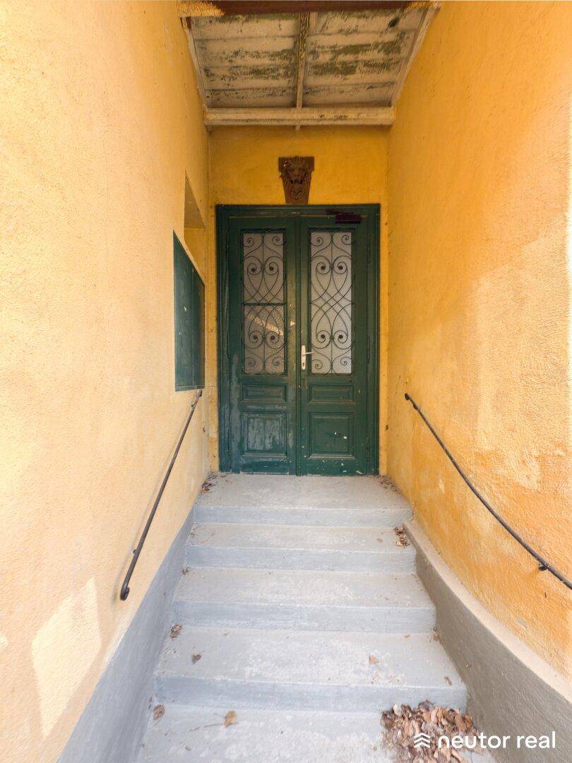 Eingangsbereich mit Treppe und einer alten grünen Doppeltür, die in das Gebäude führt.
