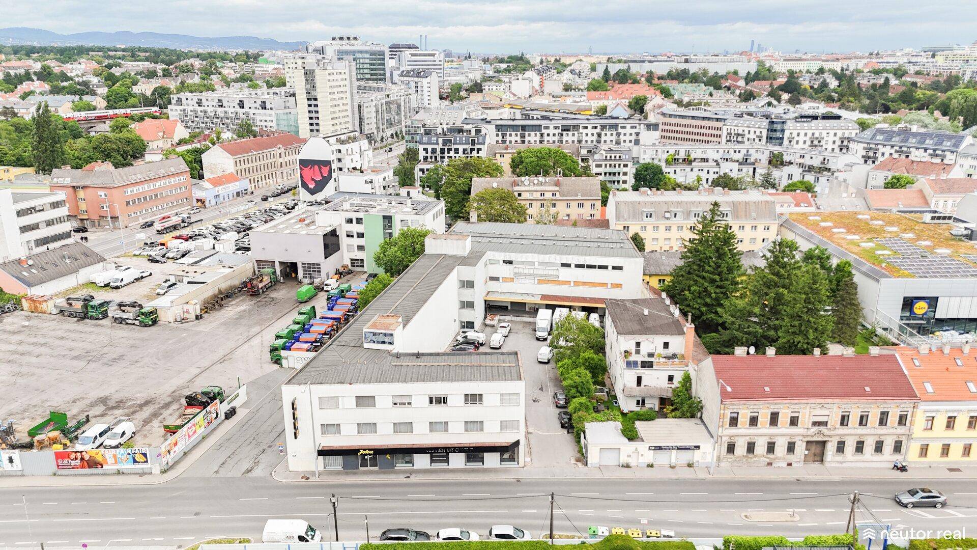 Weitläufige Luftaufnahme eines Stadtteils mit Gewerbegebäuden, Wohngebäuden und viel Grün.