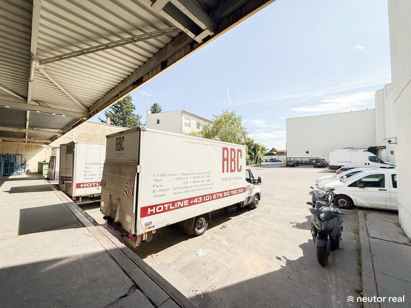 Ladebereich mit überdachter Rampe und parkenden Lieferwagen an einem sonnigen Tag.