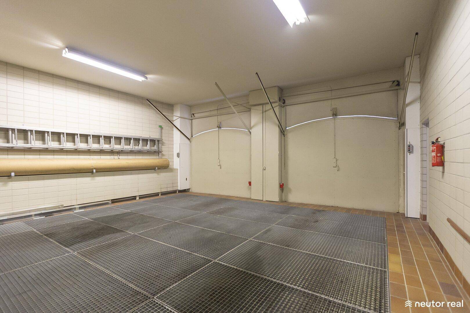 Geräumige Garage mit Fliesenboden, weißen Wänden und zwei Garagentoren.