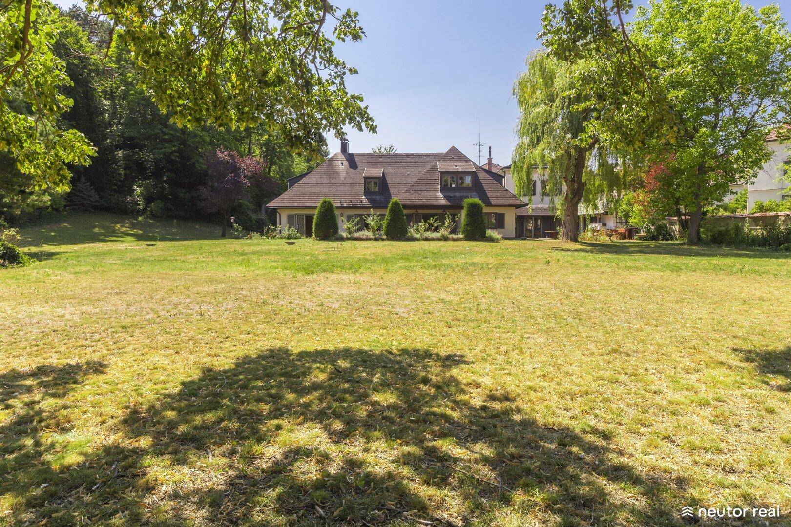 Weitläufiger Garten mit großem Rasen und dem Haus im Hintergrund unter Bäumen.