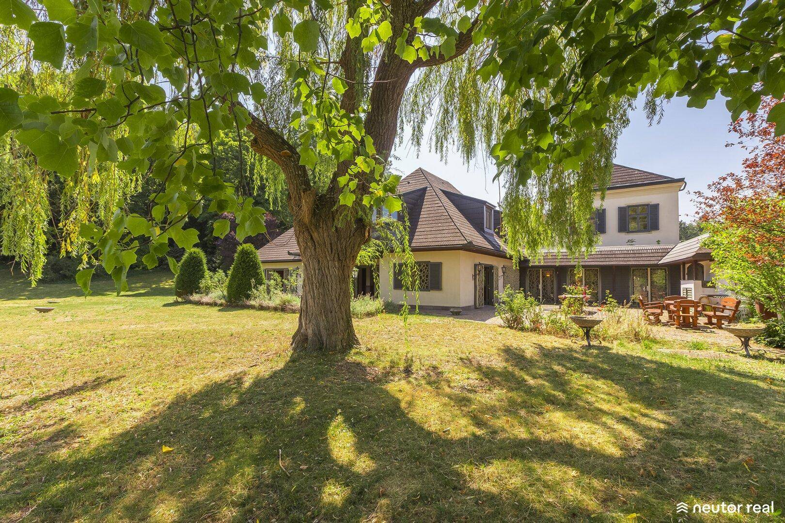 Weitläufiger Garten mit altem Baumbestand und Sitzbereich im Freien.