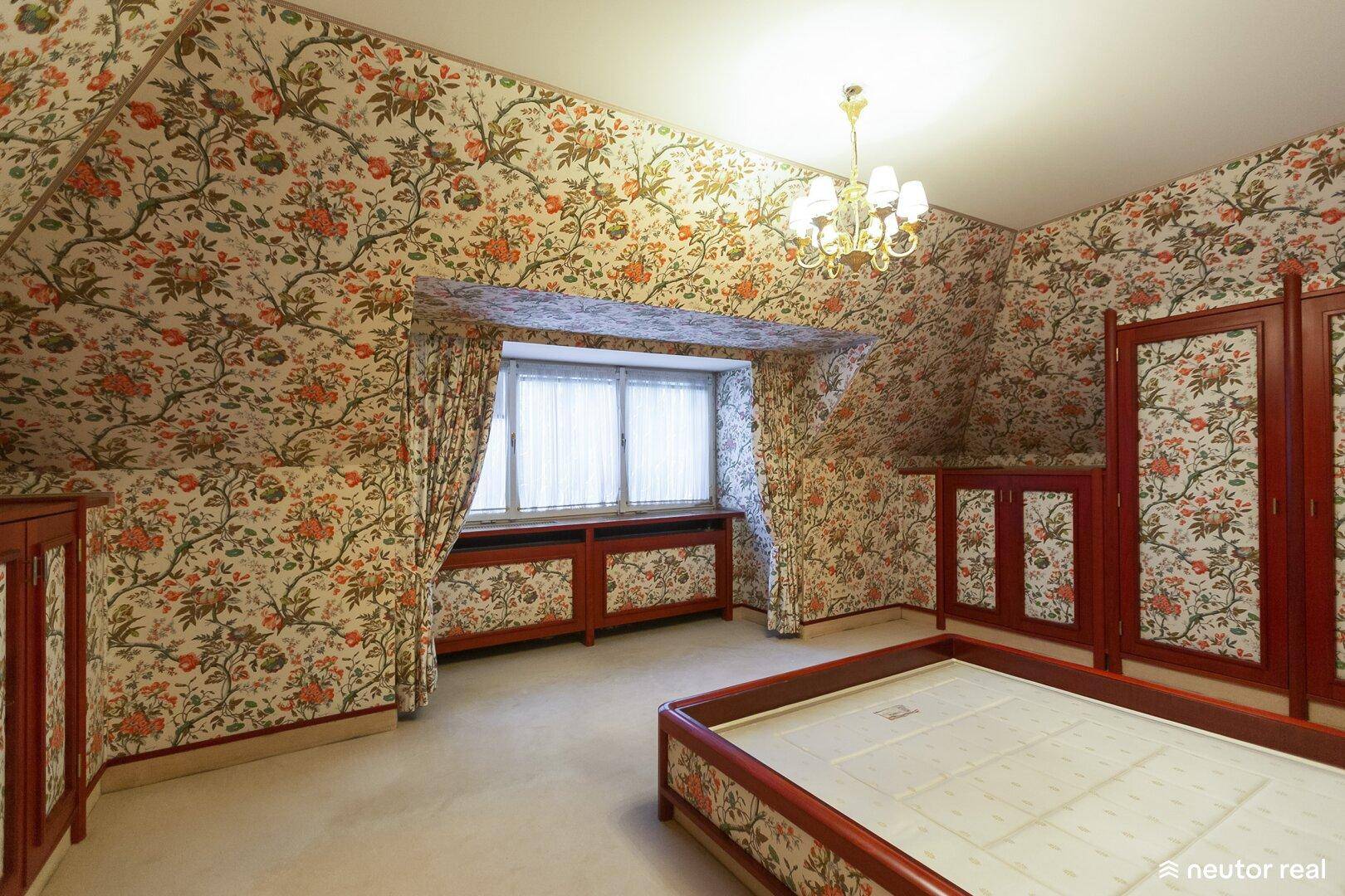 Schlafzimmer mit auffälliger Blumentapete, Teppichboden und Dachschräge.