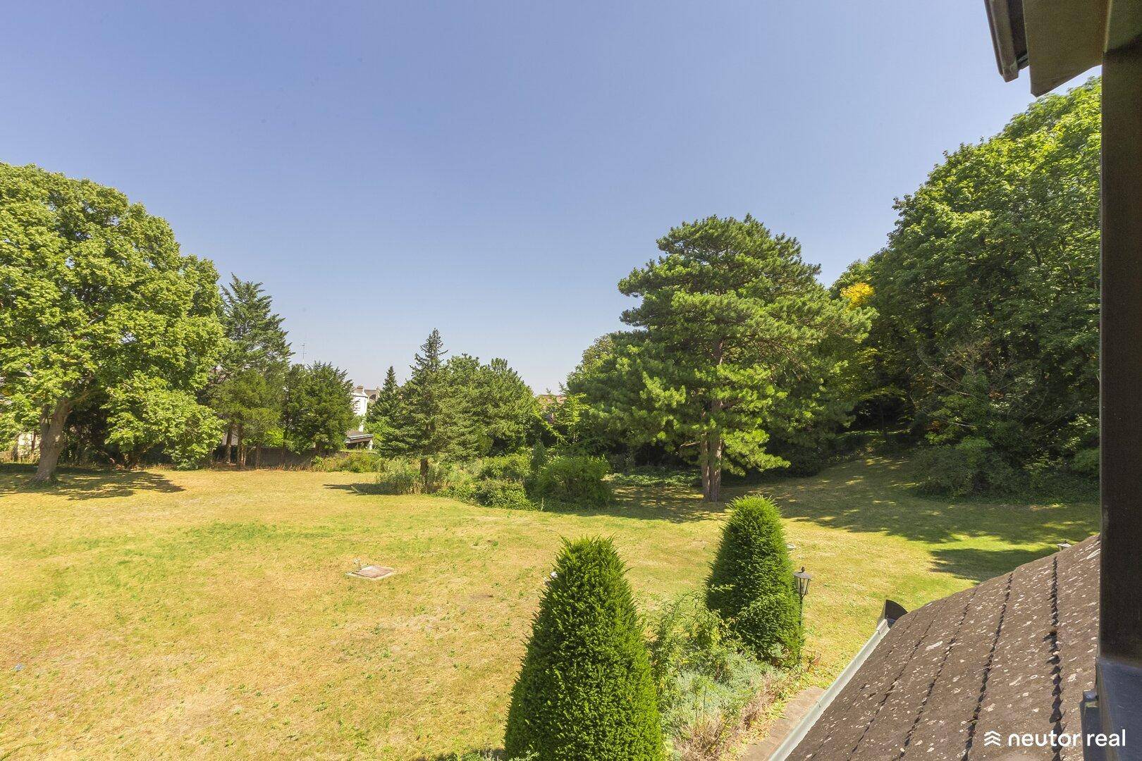 Weitläufiger Gartenbereich mit üppigem Grün und Blick auf die umliegende Natur unter klarem Himmel.