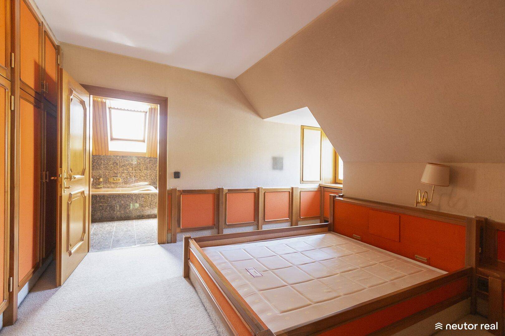 Schlafzimmer mit orangefarbenen Akzenten, Teppichboden und Zugang zum Bad.