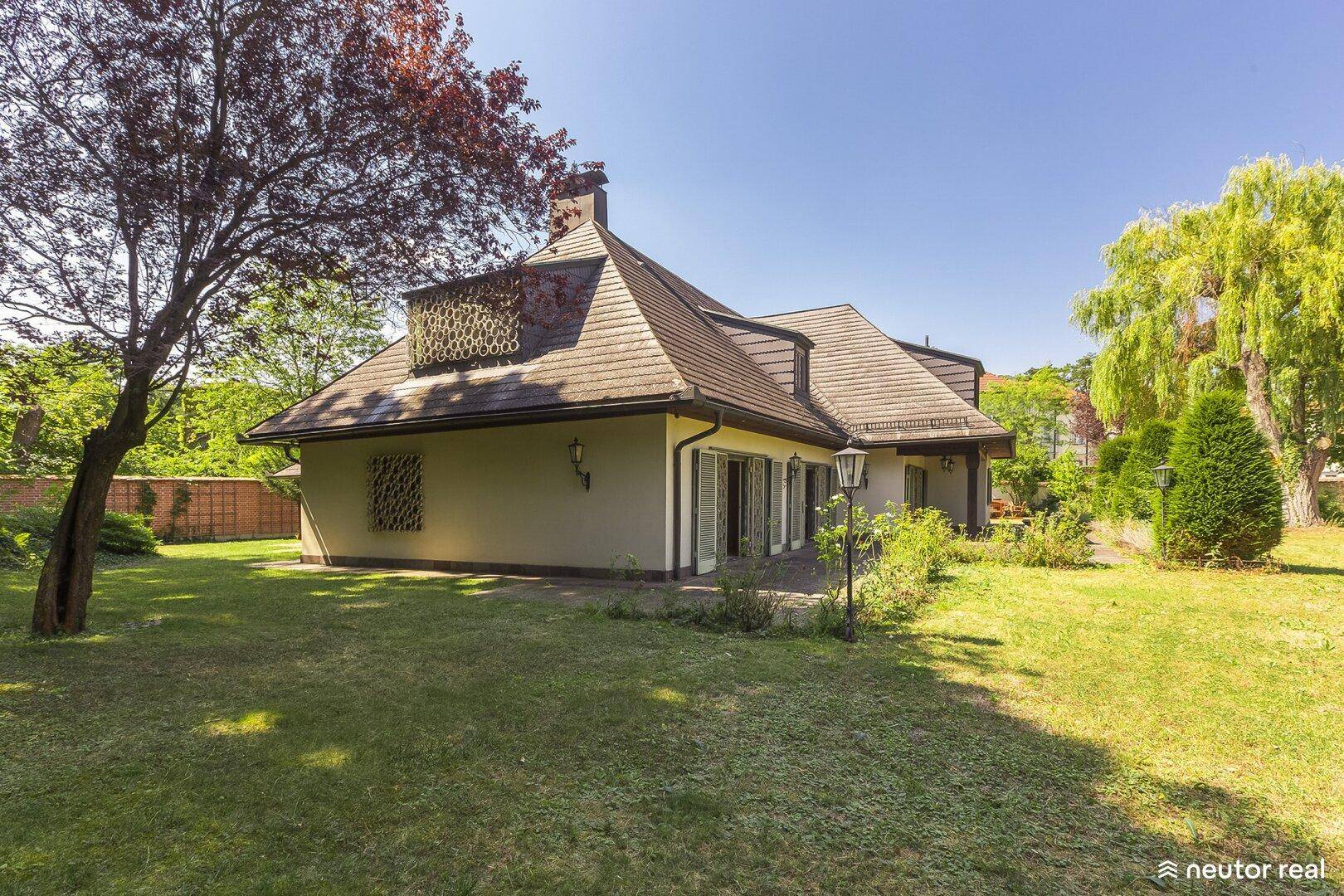 Charmantes Landhaus mit Mansarddach und weitläufigem Gartenbereich unter strahlendem Sonnenschein.