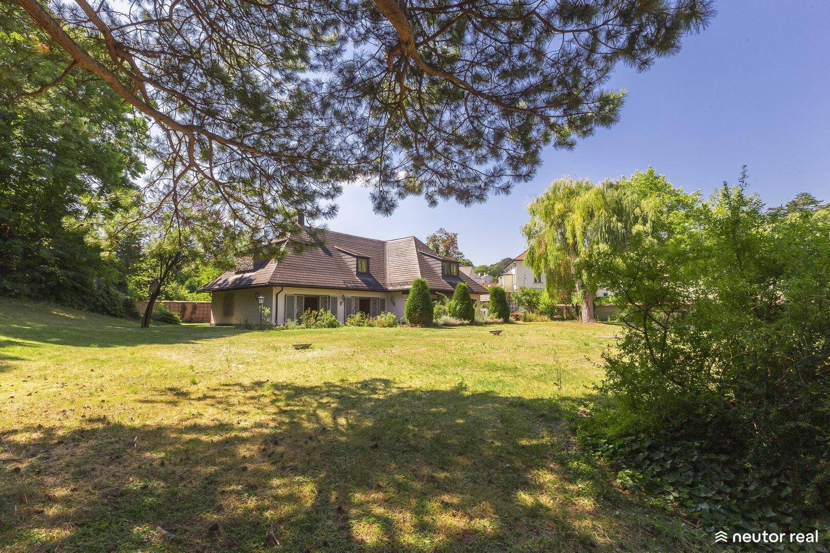 Großzügiger Garten mit altem Baumbestand und Blick auf das elegante Landhaus im Hintergrund.