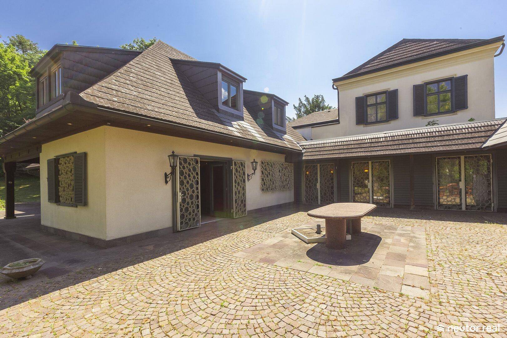 Große gepflasterte Terrasse mit dekorativem Muster und Blick auf die elegante Hausfassade.