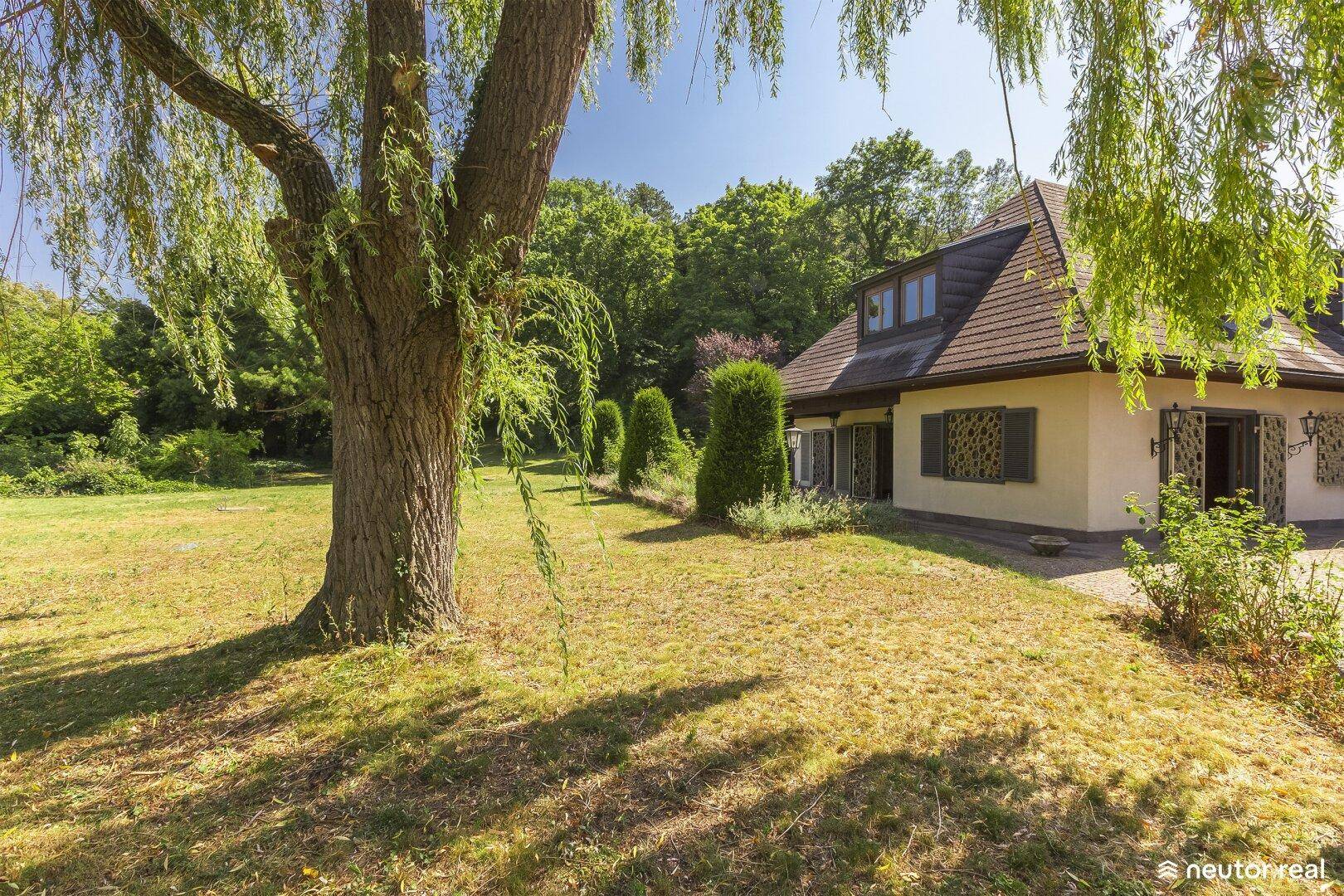 Großzügiger Gartenbereich mit altem Baumbestand und Blick auf das Landhaus mit Mansarddach.