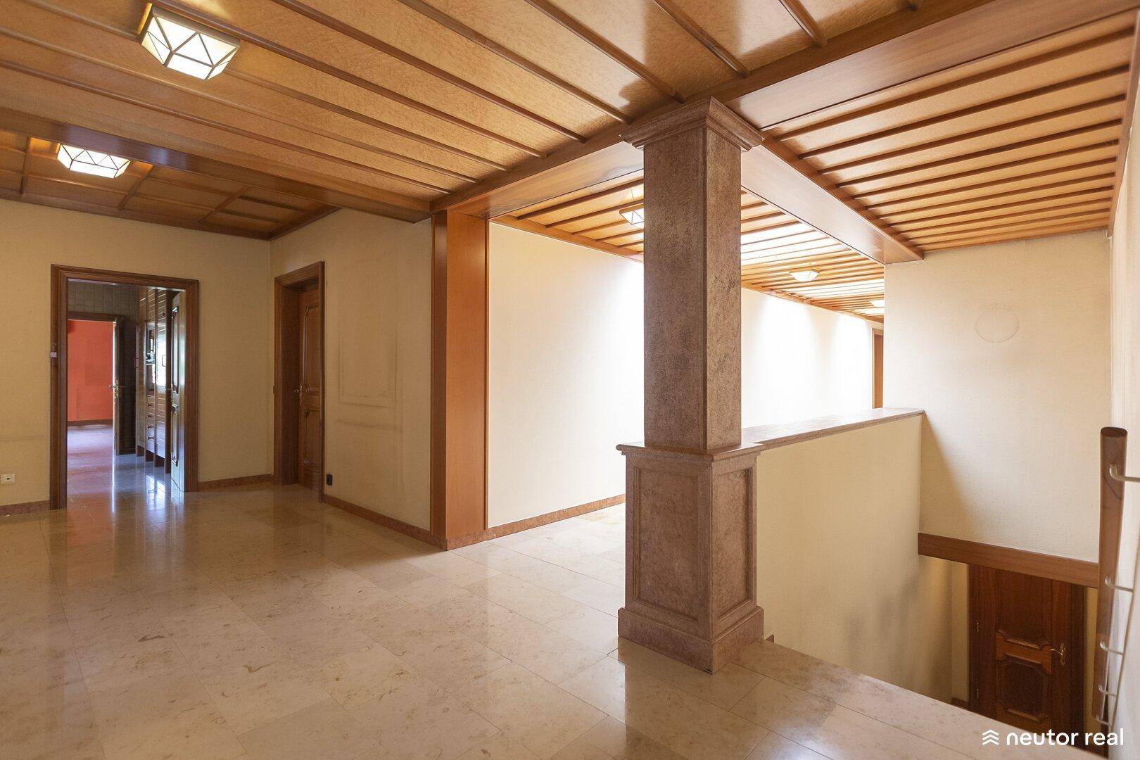 Heller Flur mit Holzdecke, Marmorboden und Säulen, die den Raum strukturieren.
