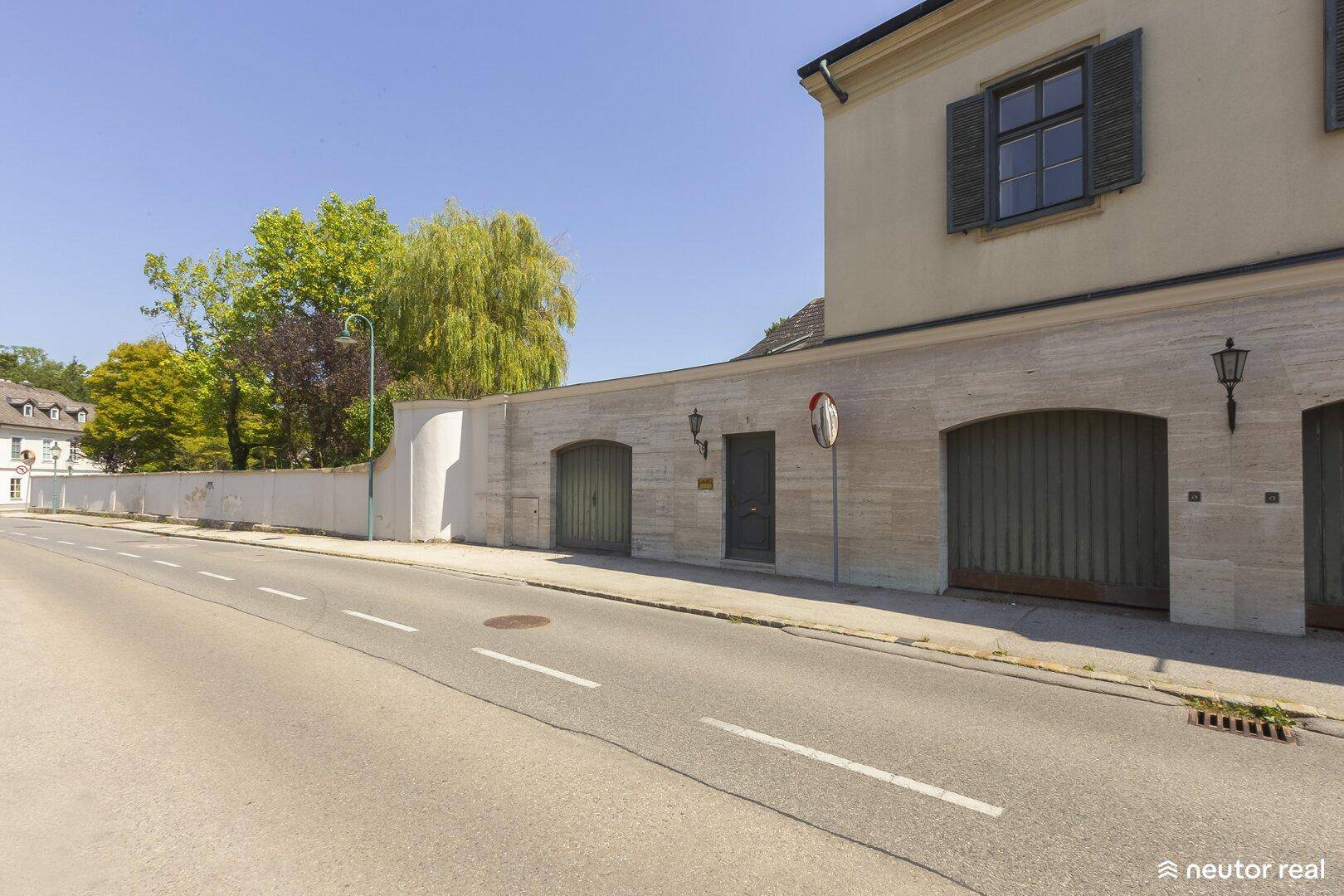 Elegante Straßenfassade des Anwesens mit Natursteinverkleidung und integrierten Garagentoren.