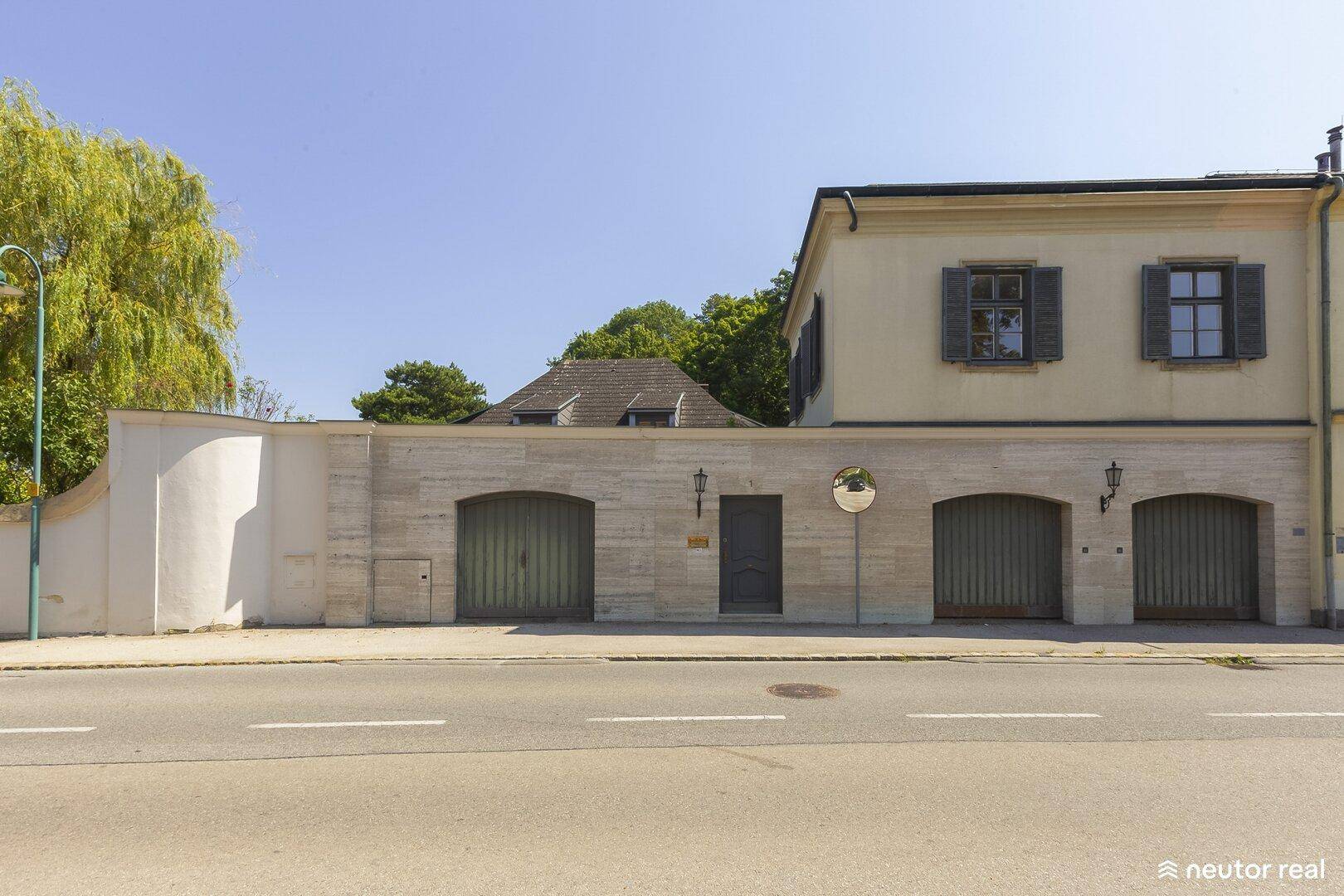 Repräsentative Straßenansicht des Anwesens mit Natursteinmauer und mehreren Garagentoren.