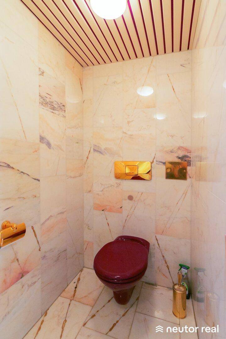 Separate Toilette mit Marmorfliesen, Holzdecke und bordeauxrotem WC.