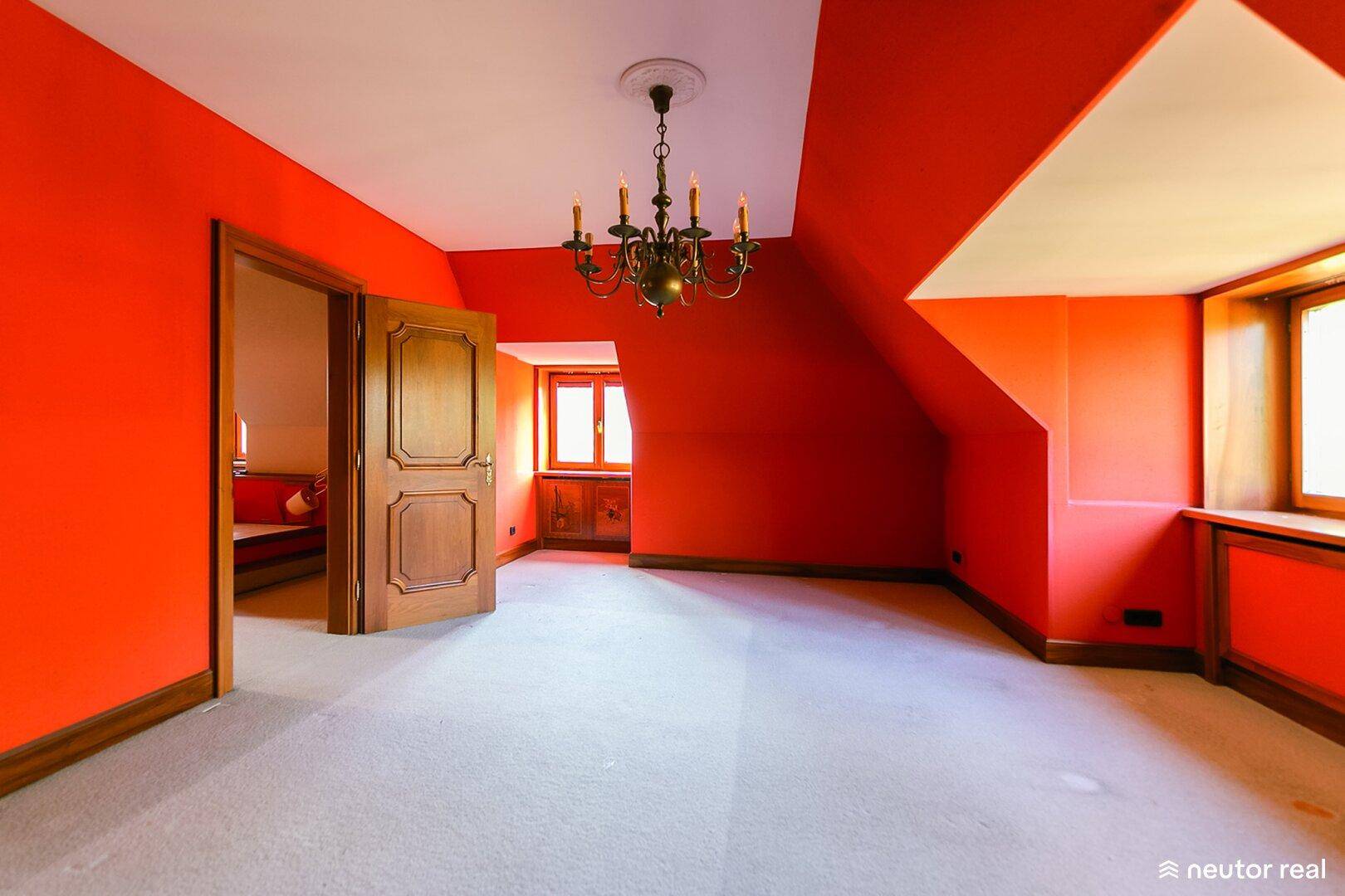 Heller Raum mit roten Wänden, Dachschrägen und einem eleganten Kronleuchter.