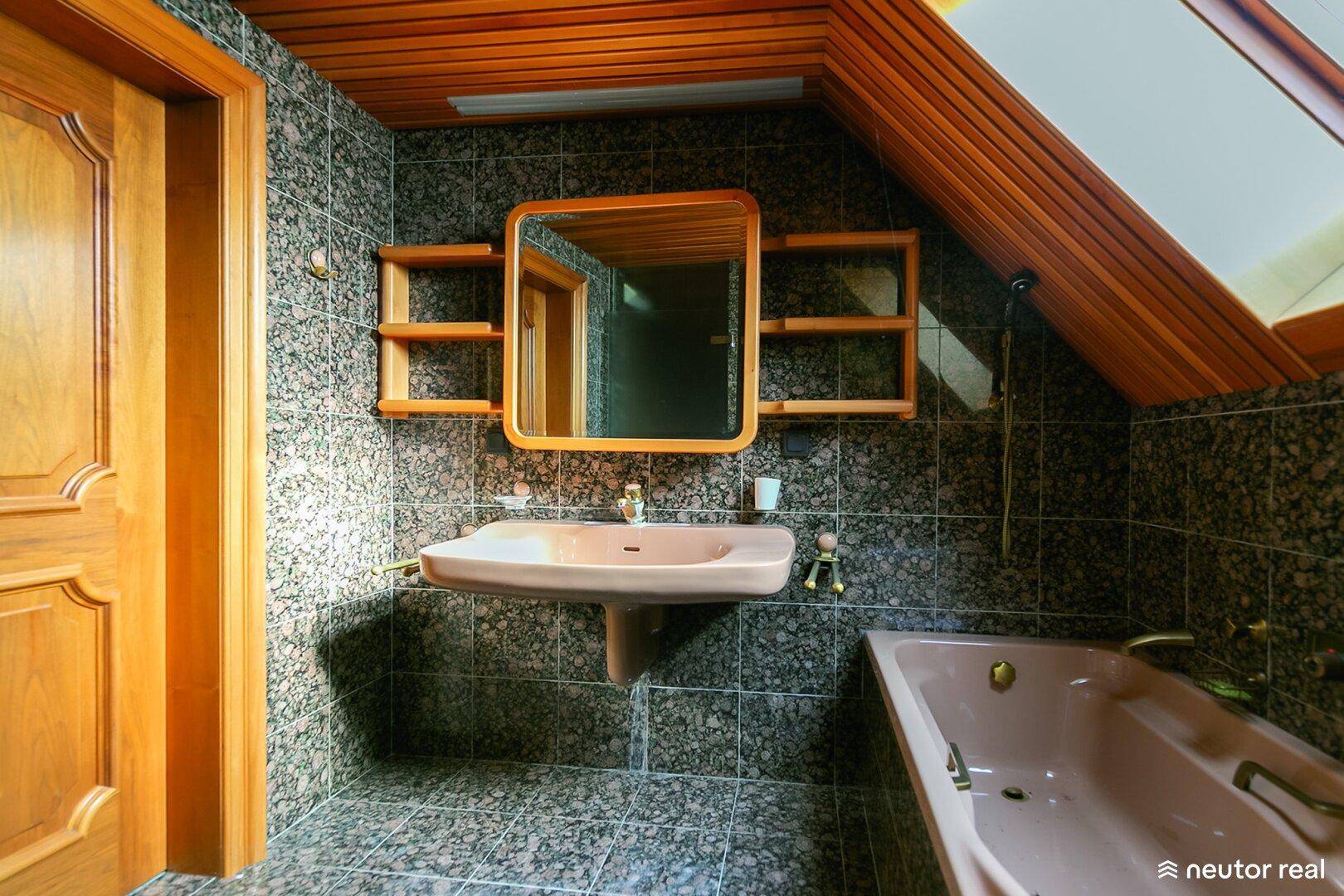 Badezimmer mit dunklen Granitfliesen, Holzdecke, rosa Badewanne und Waschbecken.