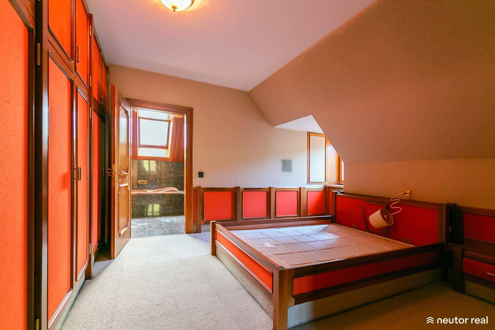 Schlafzimmer mit Dachschrägen, Einbauschränken und Zugang zu einem Badezimmer.