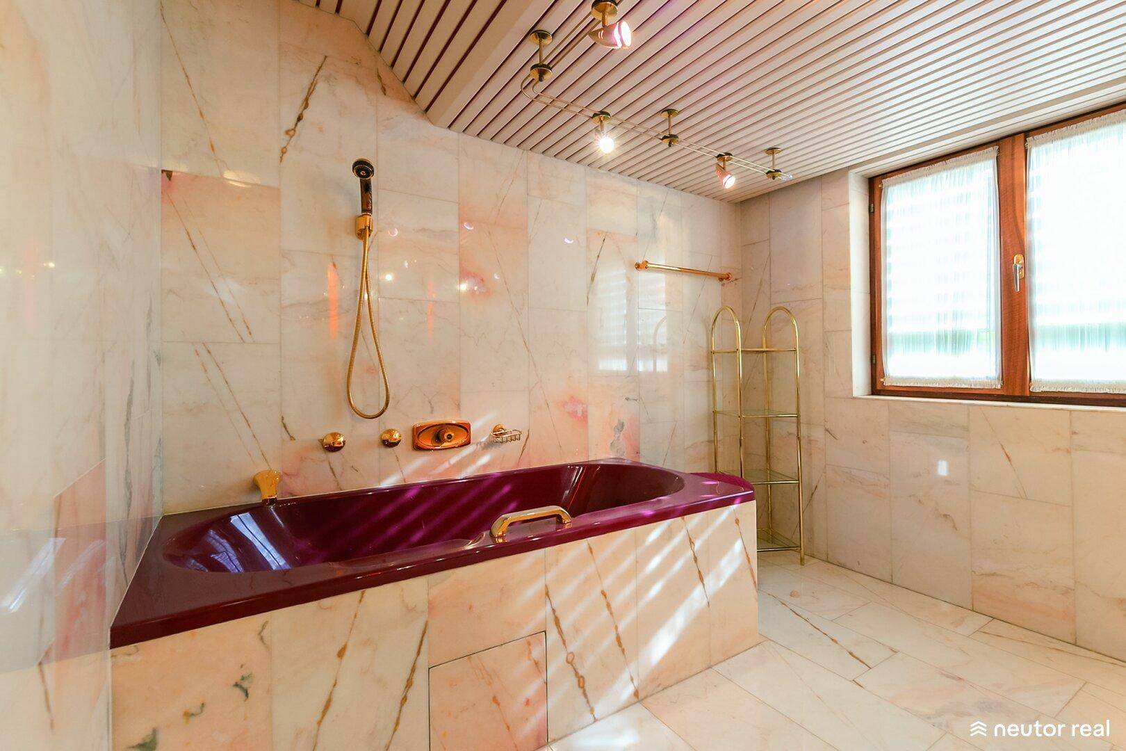 Badezimmer mit Marmorfliesen, Holzdecke und bordeauxroter Badewanne.