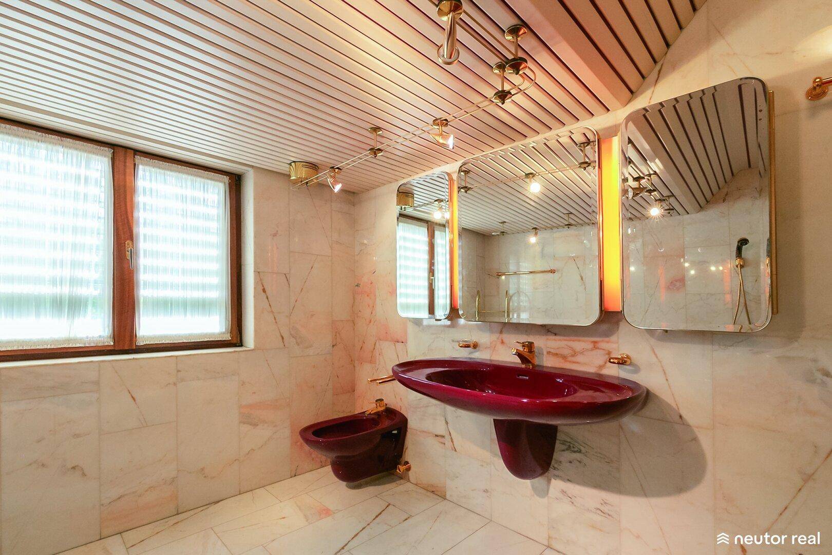 Badezimmer mit Marmorfliesen, Holzdecke und auffälligem bordeauxrotem Waschbecken.
