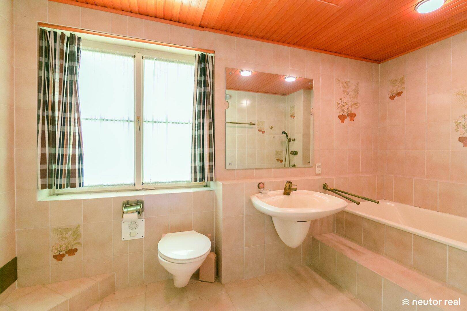 Badezimmer mit beigefarbenen Fliesen, Holzdecke, Badewanne, WC und Fenster.