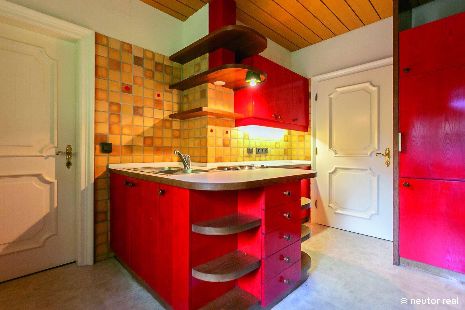Kleine Küchenzeile mit roten Schränken, Fliesenspiegel und Holzdecke.