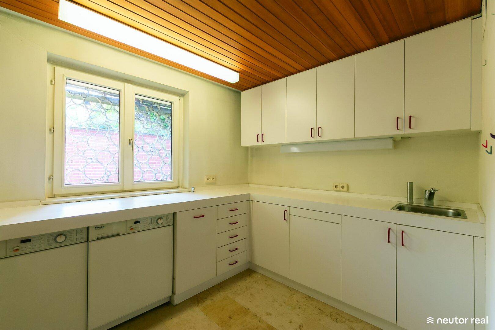 Hauswirtschaftsraum mit weißen Schränken, Spüle und Fenster.