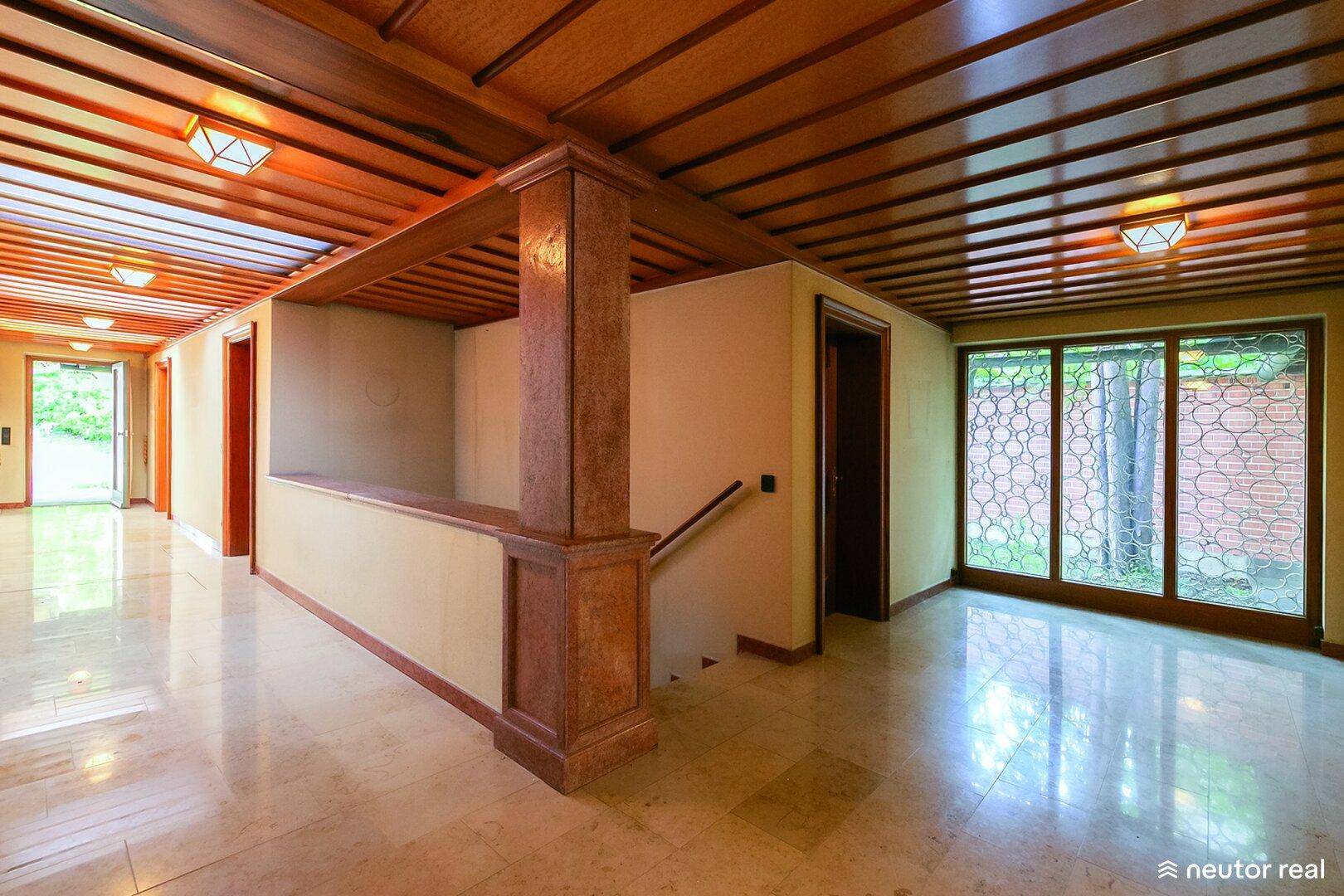 Geräumiger Eingangsbereich mit glänzendem Marmorboden, Holzdecken und Zugang zu verschiedenen Räumen.