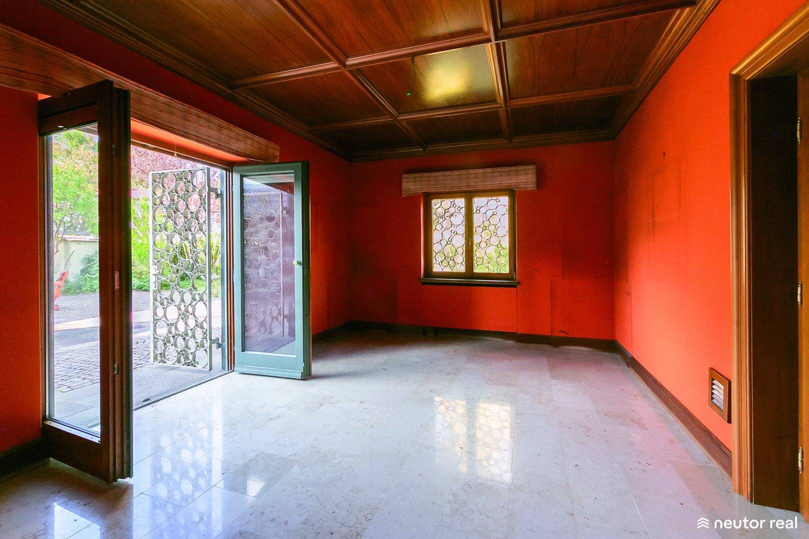 Heller Raum mit leuchtend roten Wänden, Marmorboden und Zugang zur Terrasse durch Flügeltüren.