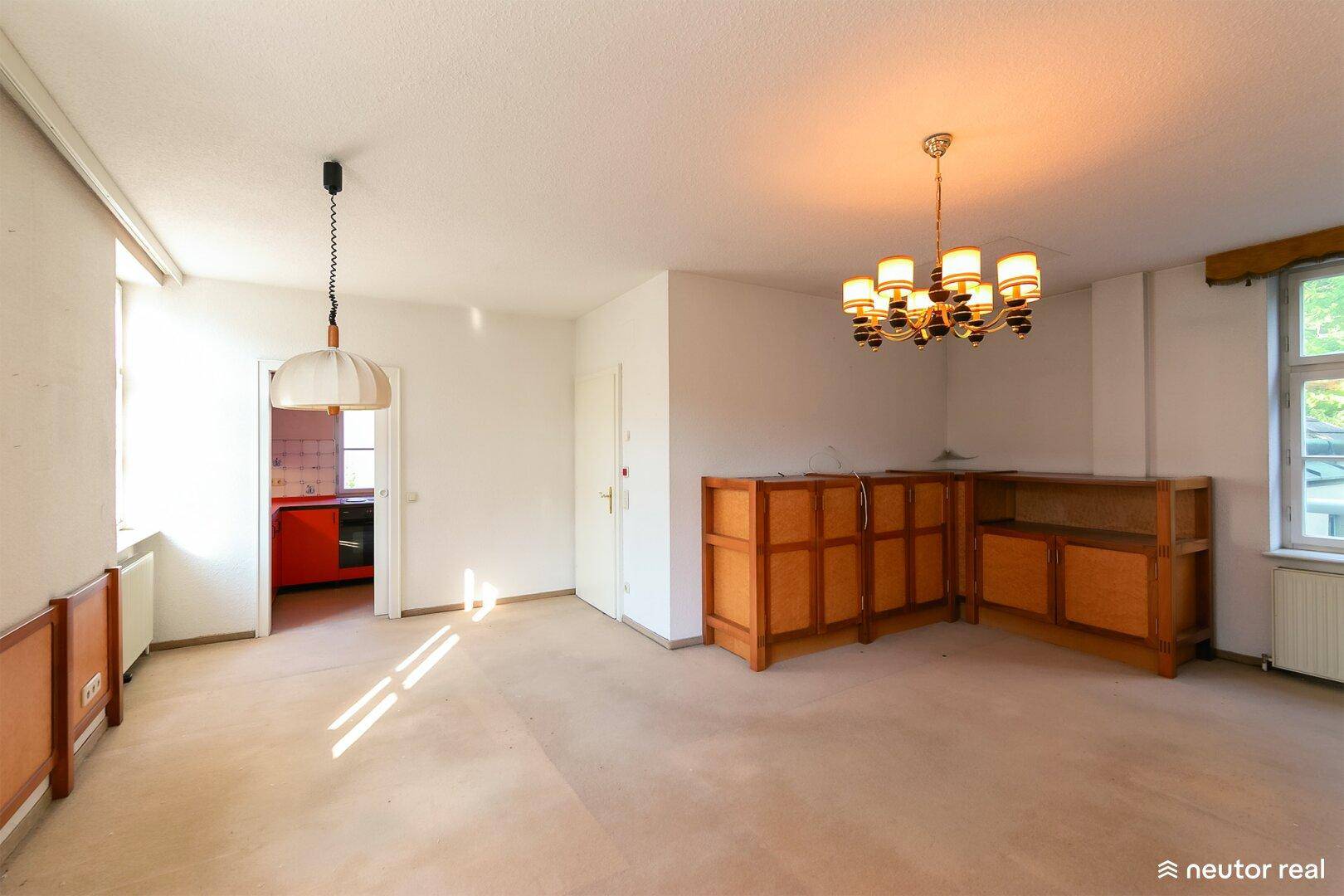 Helles Wohnzimmer mit viel Tageslicht, Kronleuchter und Zugang zur Küche.