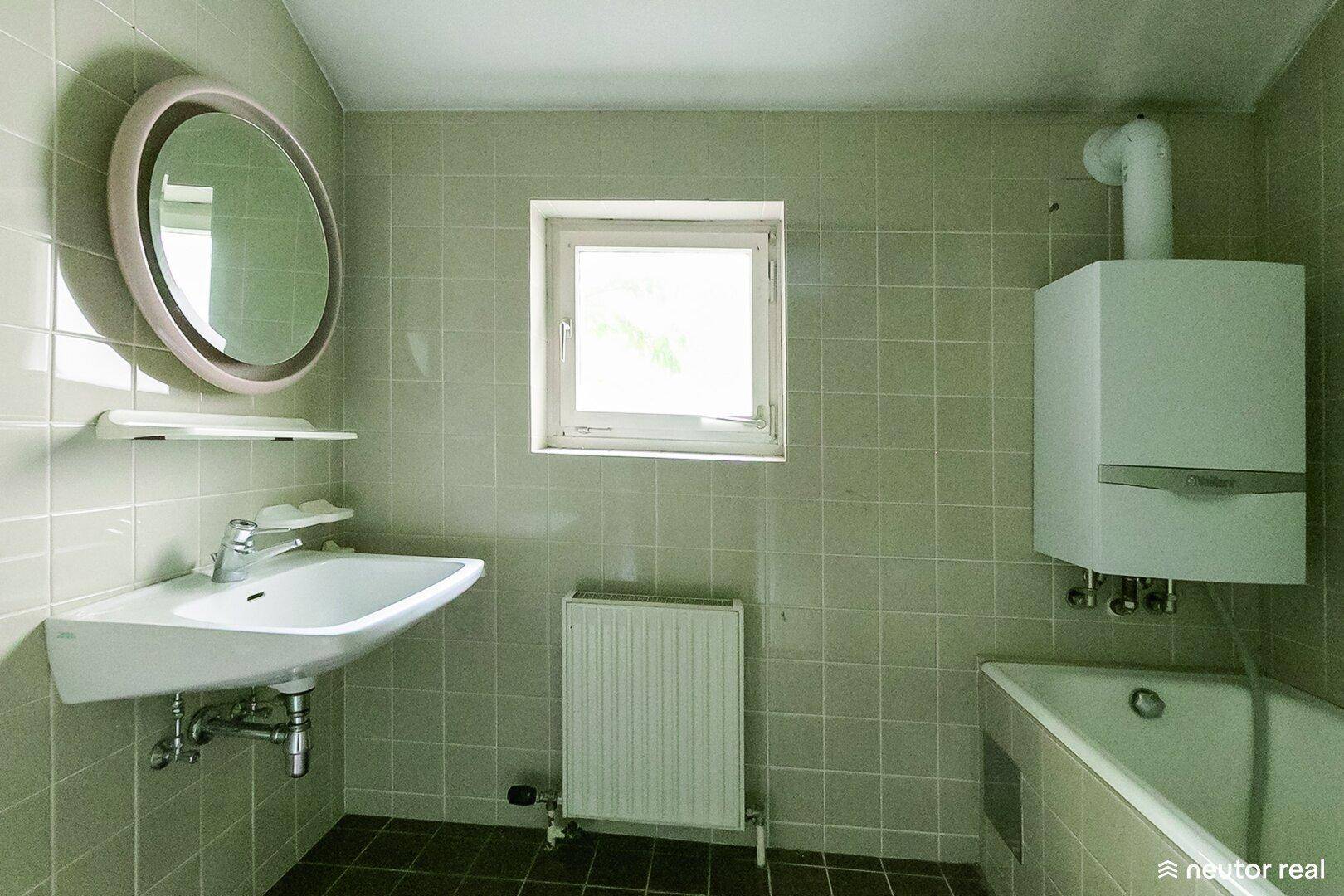 Badezimmer mit hellgrünen Fliesen, Waschbecken, Badewanne und Fenster.