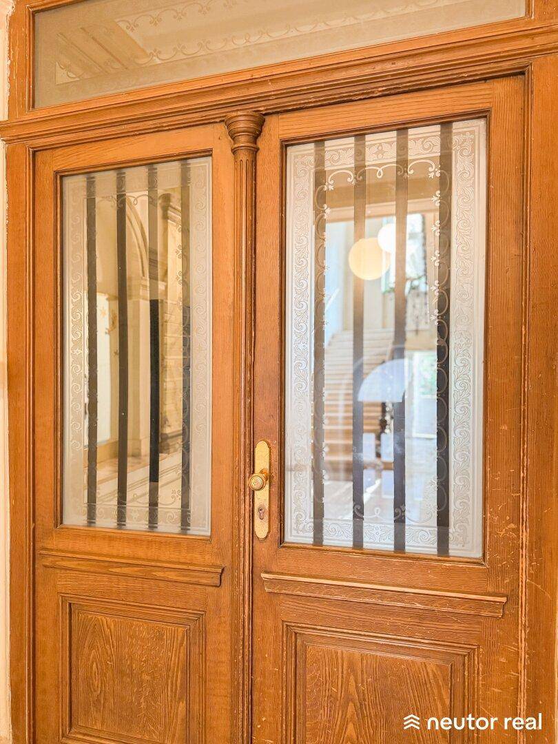 Detailaufnahme einer verzierten Holztür mit Glaseinsätzen und Blick ins Treppenhaus.