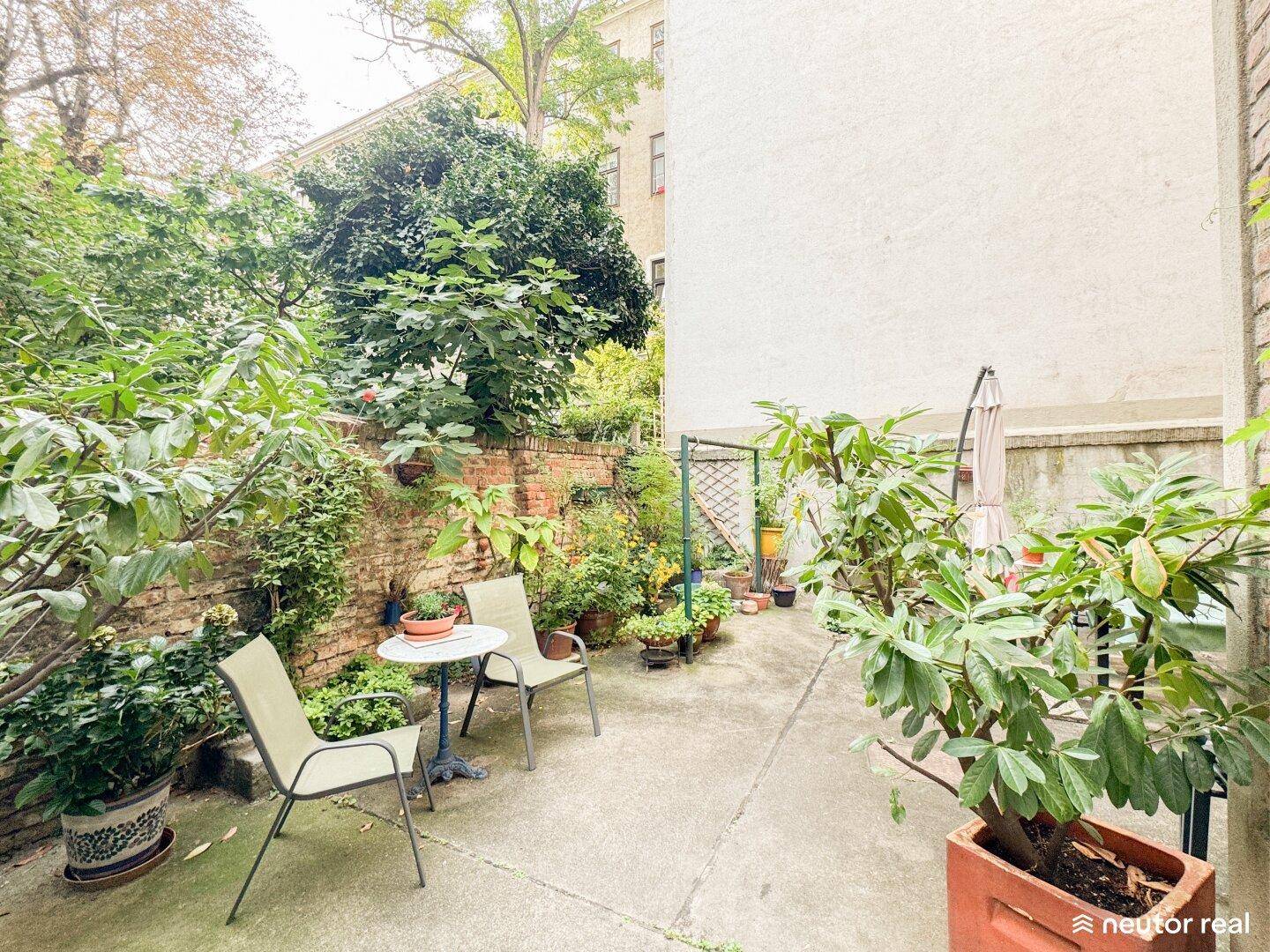 Kleiner, begrünter Innenhof mit Sitzgelegenheiten und vielen Pflanzen, ideal zum Entspannen.