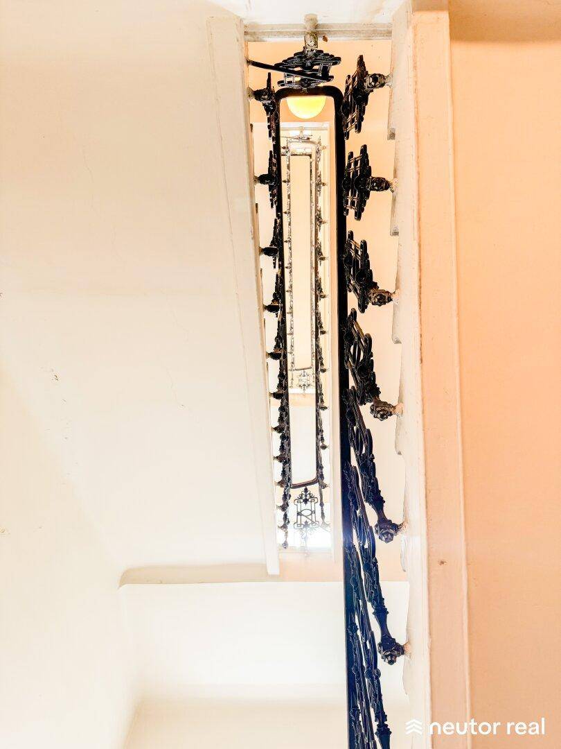 Blick von oben auf ein elegantes Treppenhaus mit kunstvollem schmiedeeisernem Geländer.