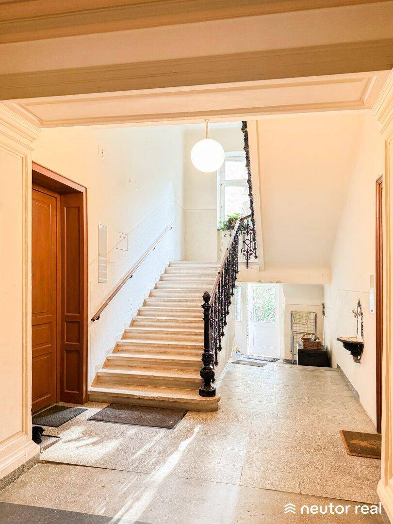 Heller Eingangsbereich mit breiter Steintreppe, schmiedeeisernem Geländer und hohen Decken.