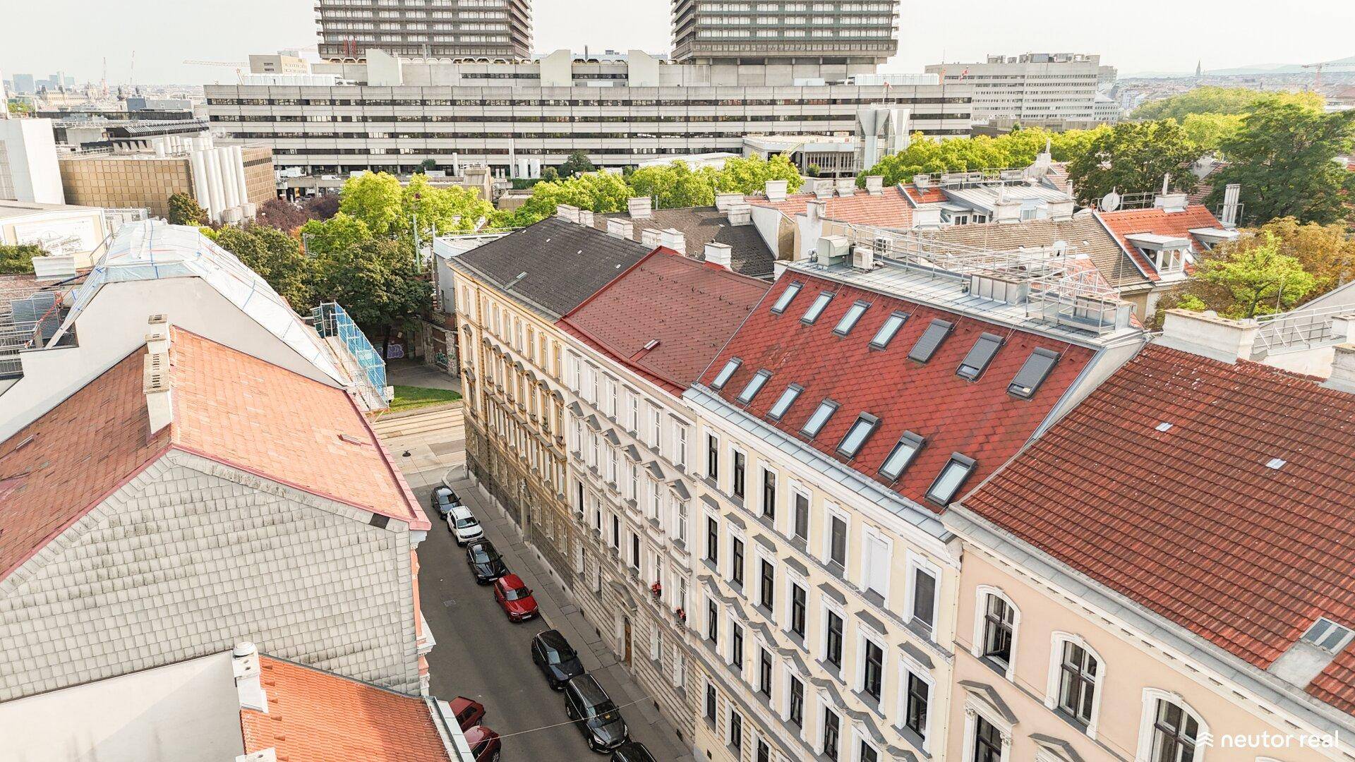 Dachlandschaft einer Stadt mit roten Ziegeldächern, darunter eine Straße mit parkenden Autos.