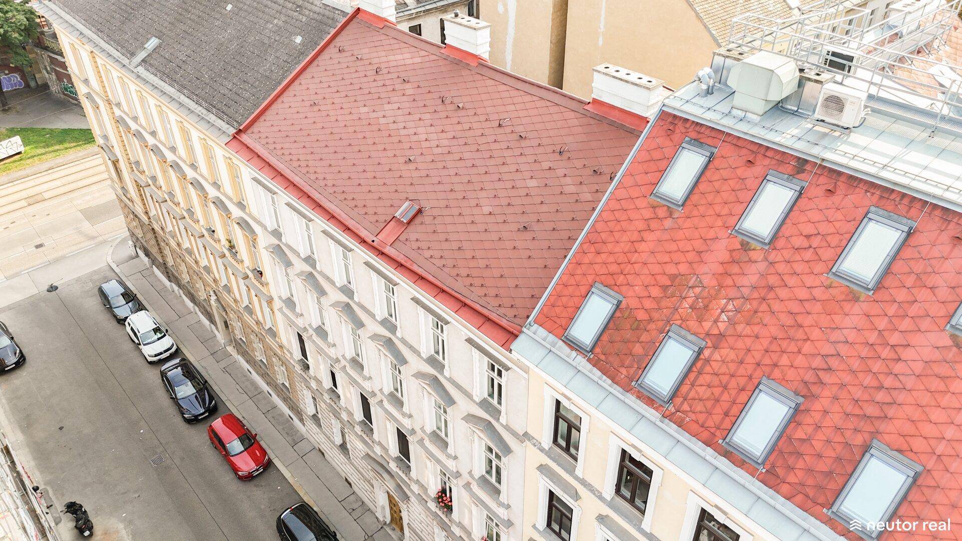 Nahaufnahme einer städtischen Dachlandschaft mit roten Ziegeldächern und parkenden Autos auf der Straße.