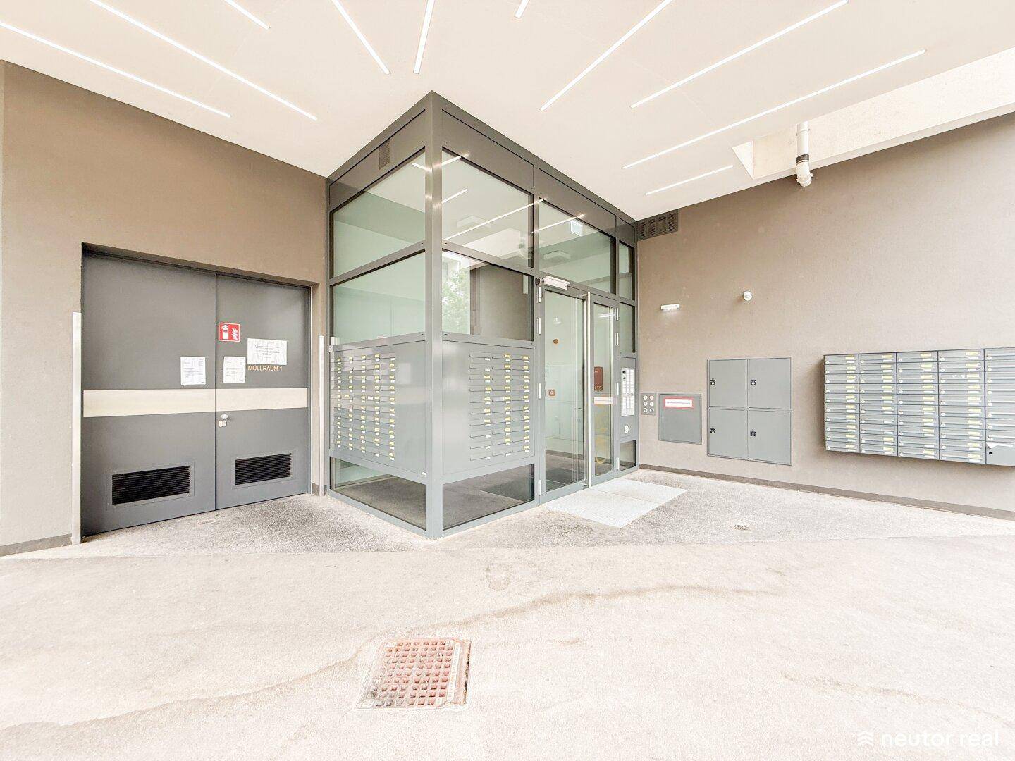 Moderner Eingangsbereich mit Briefkästen und verglaster Lobby in einem Wohngebäude.