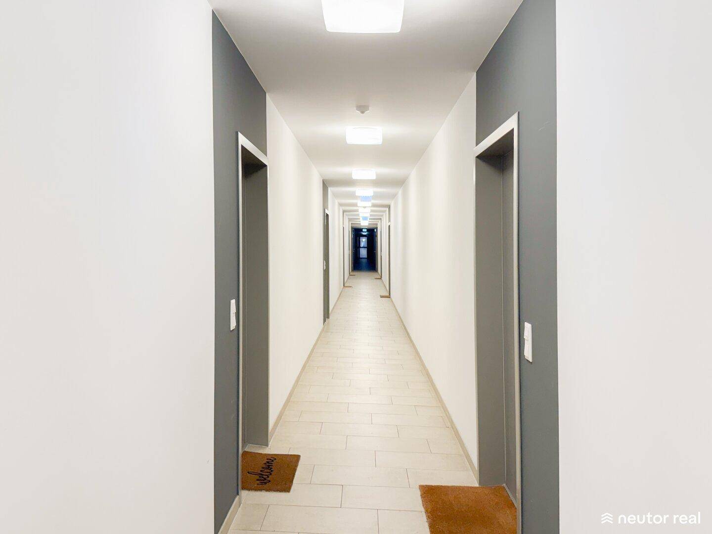 Langer, heller Flur mit Fliesenboden und Türen zu den einzelnen Wohneinheiten.