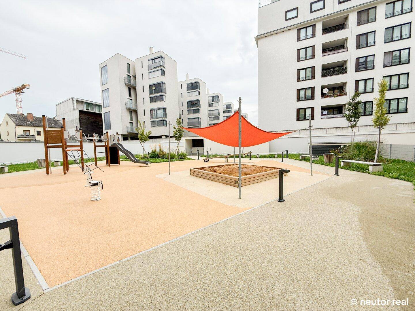 Moderner Kinderspielplatz mit Sandkasten, Rutsche und Sonnensegel, umgeben von Wohngebäuden.