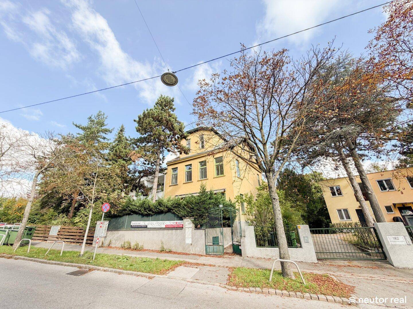 Gelbe Villa mit grünen Fensterrahmen und umgebender Vegetation an einem sonnigen Tag.