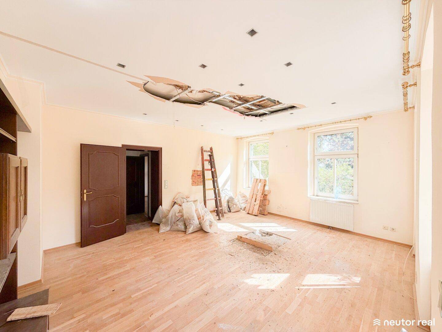 Großer Raum mit Holzboden und beschädigter Decke, bereit für umfassende Renovierungsarbeiten.
