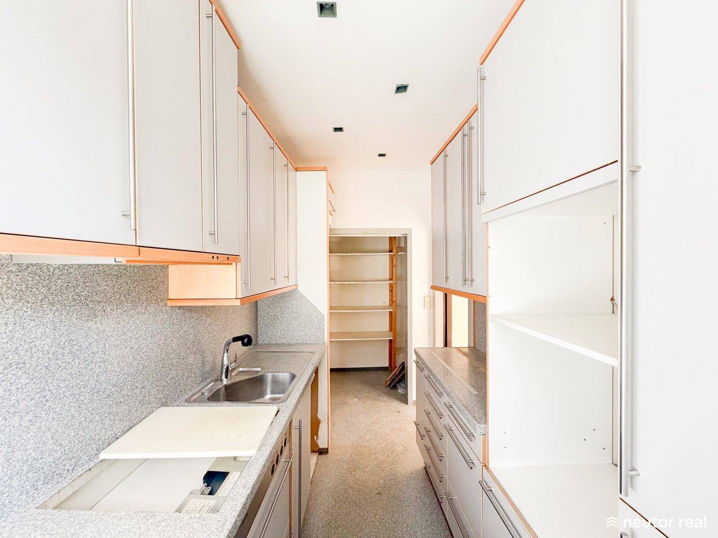 Schmale Küche mit weißen und holzfarbenen Schränken, bereit für eine Modernisierung.