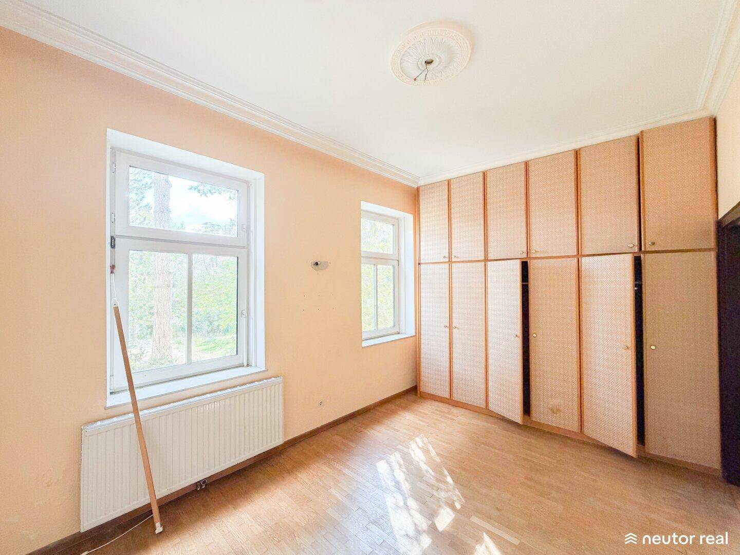 Schlafzimmer mit Holzboden, großen Fenstern und eingebauten Kleiderschränken an einer Wand.